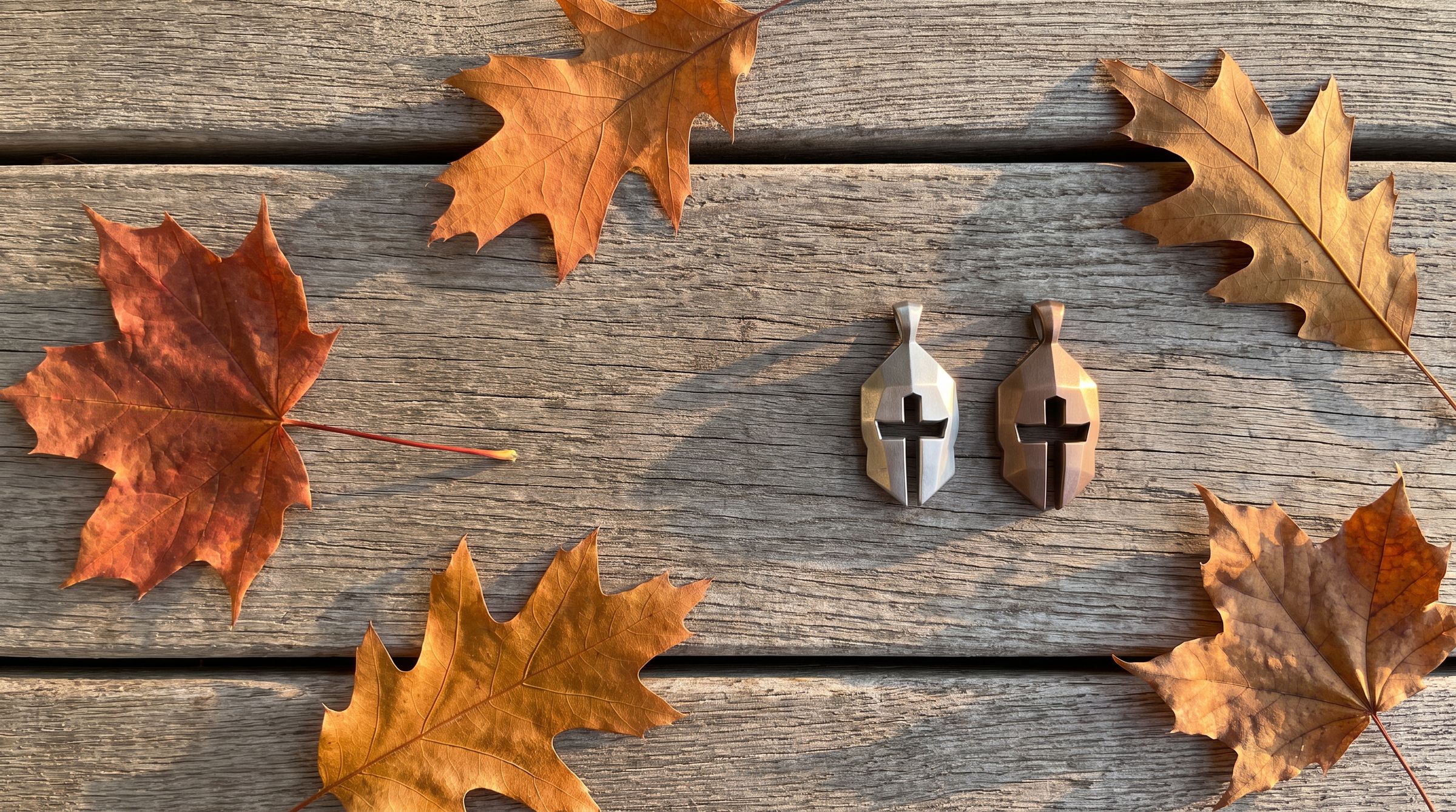 The Cross & Helm pendant in 99.9% silver and in bronze among fallen autumn leaves