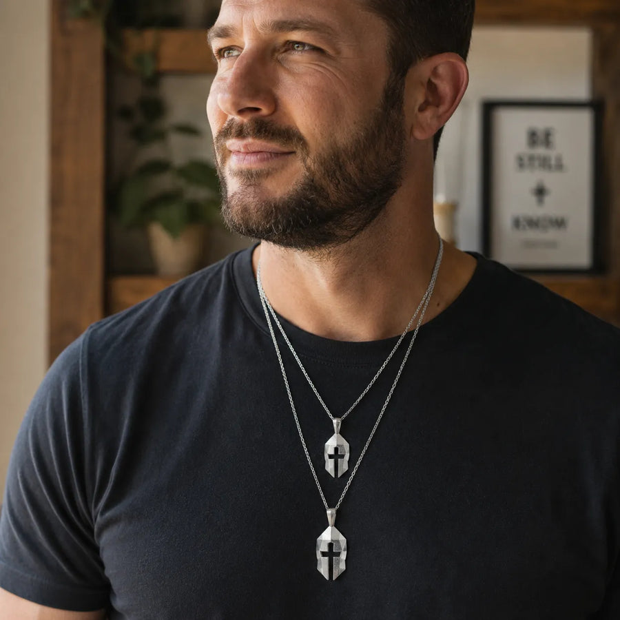 Man wearing two sterling silver Cross & Helm pendants on chains, featuring a warrior's helm and cross design. alternate view