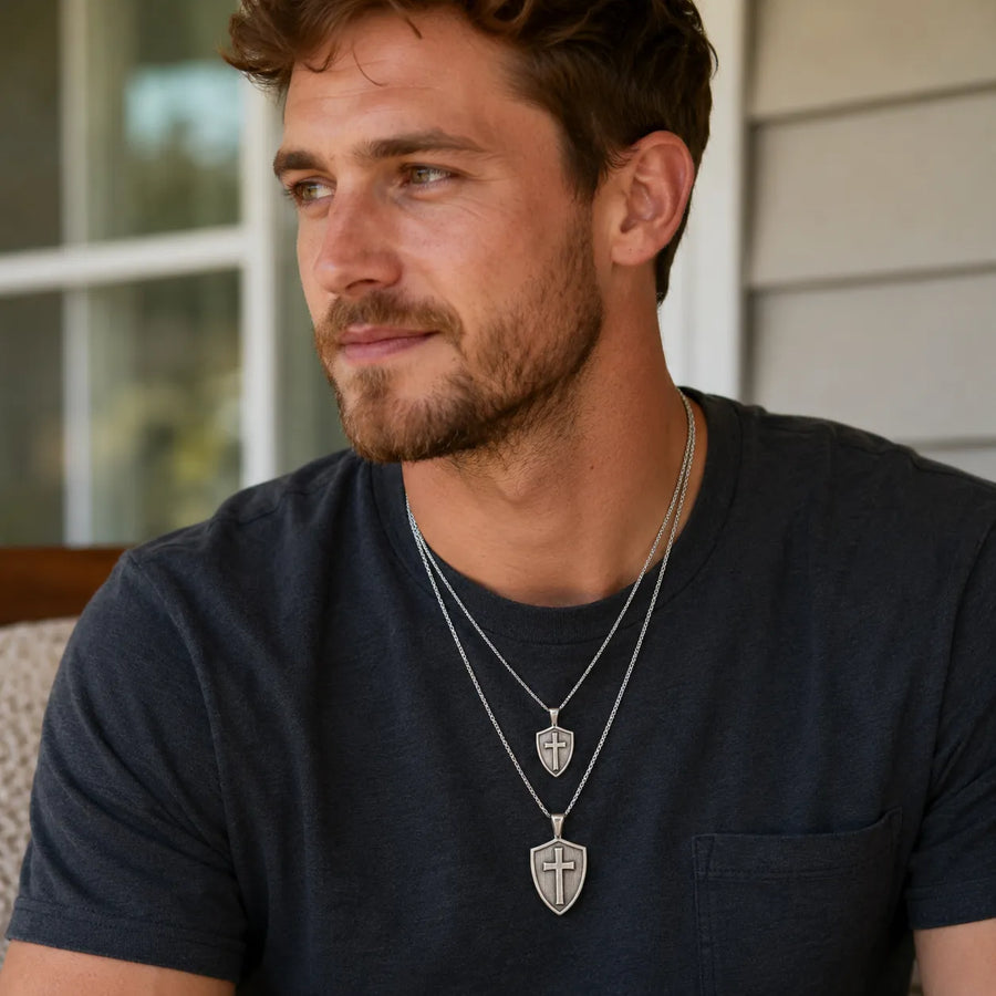 Man wearing two sterling silver Cross & Shield pendants on chains, one large and one small. alternate view