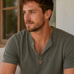 Man wearing two bronze Cross & Shield pendants, one smaller cross and one larger shield, on chains.