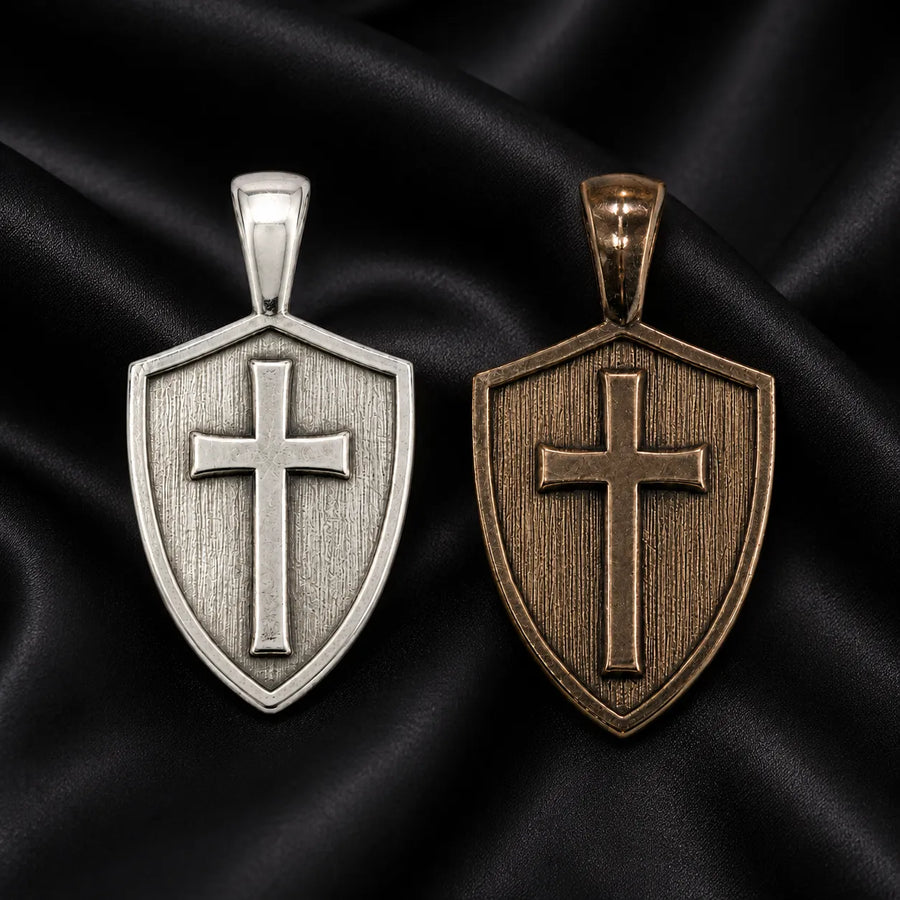 Two hand-finished Cross & Shield pendants: one sterling silver, one bronze, on black silk.