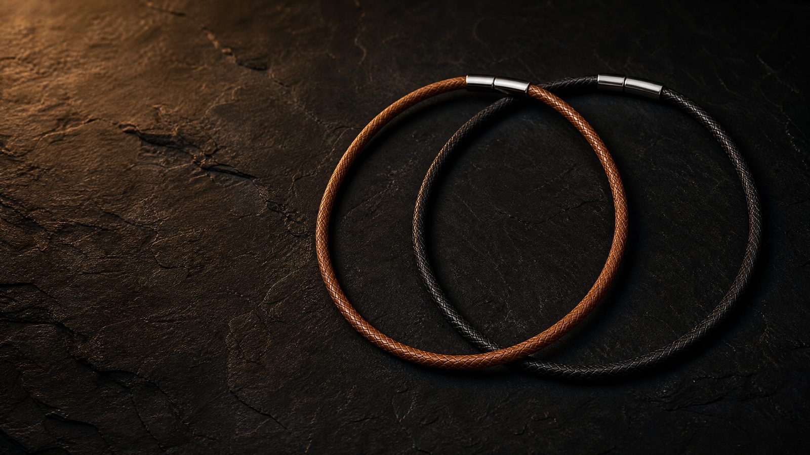 Cross & Helm brown and black braided leather necklaces with gold clasps on dark leather